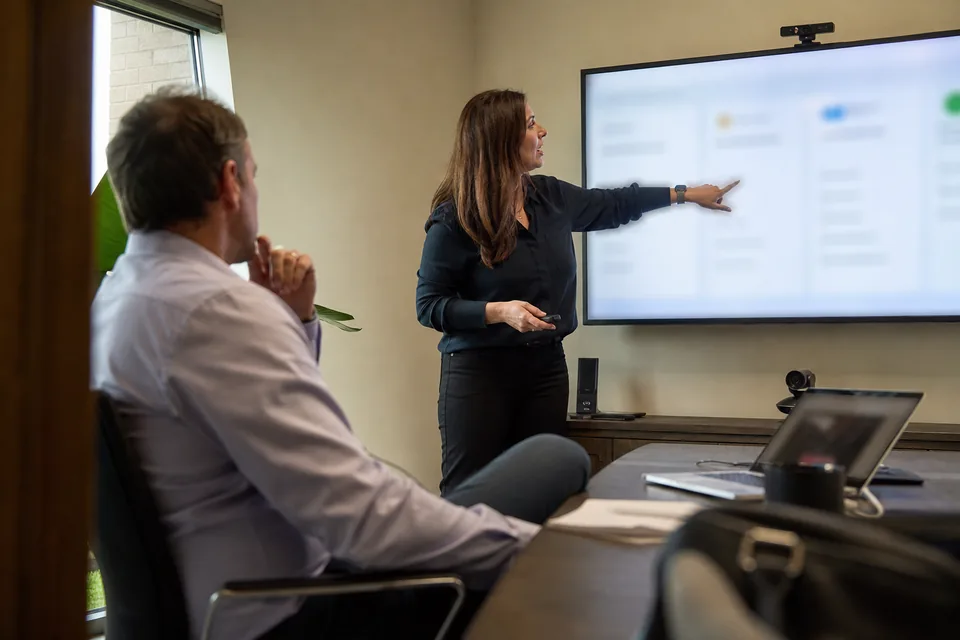 HR lead presenting a performance software shortlist to a finance executive in a conference room