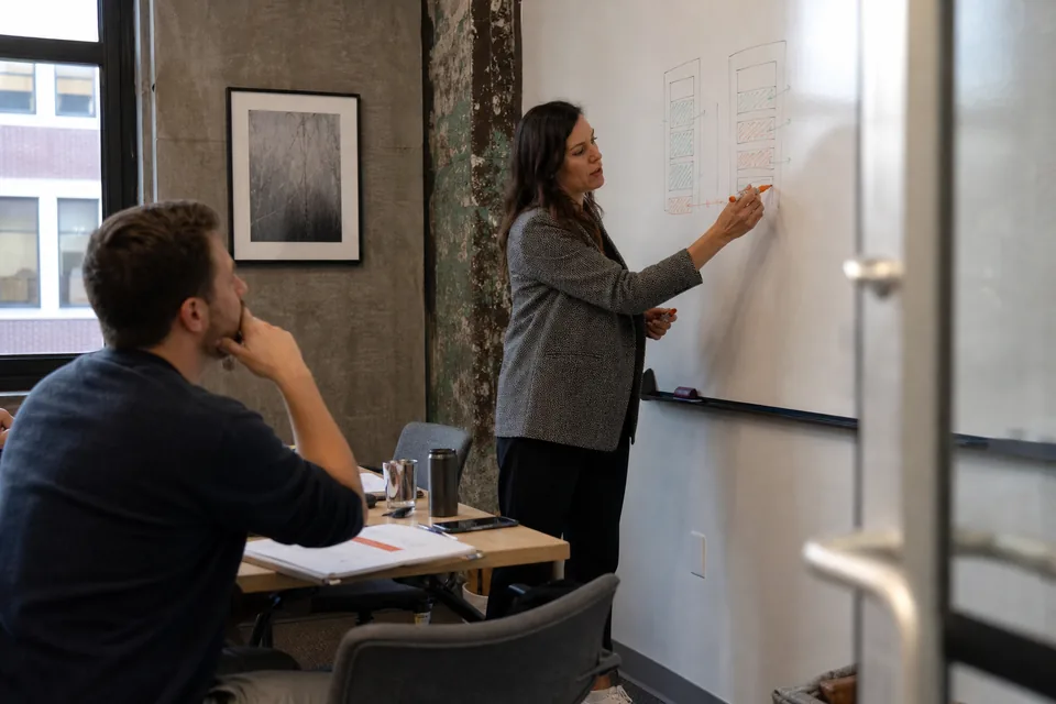 People operations director sketching a seat-count cost comparison on a whiteboard for a finance colleague