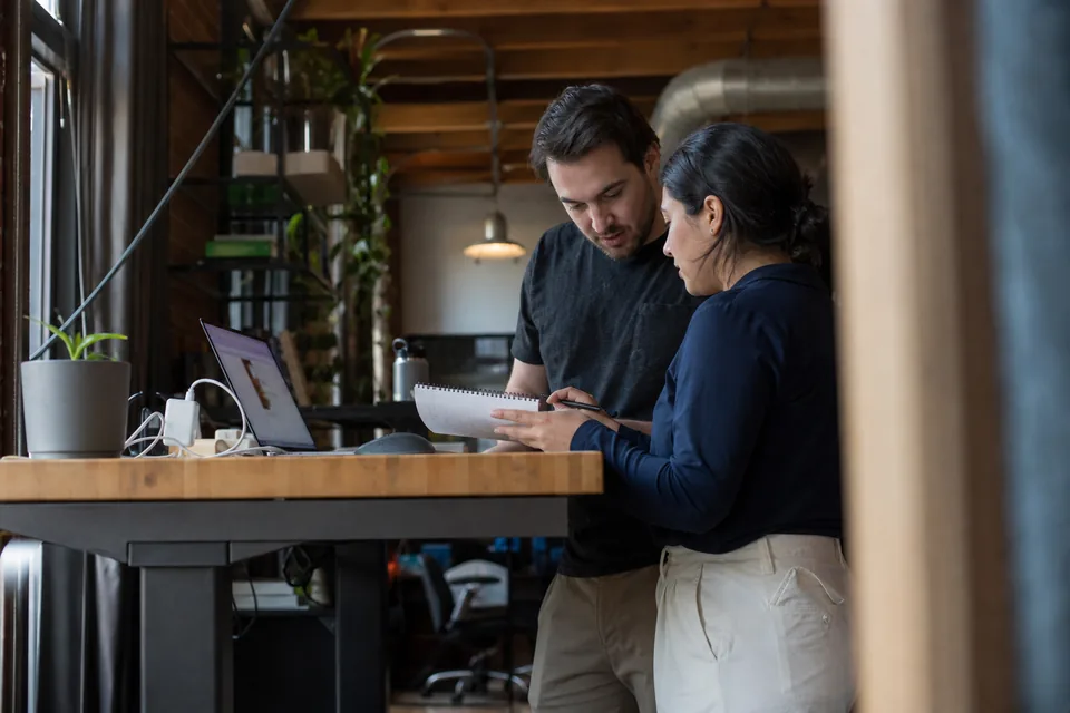 Startup founder and first HR hire working out annual software cost on a notebook at a standing desk